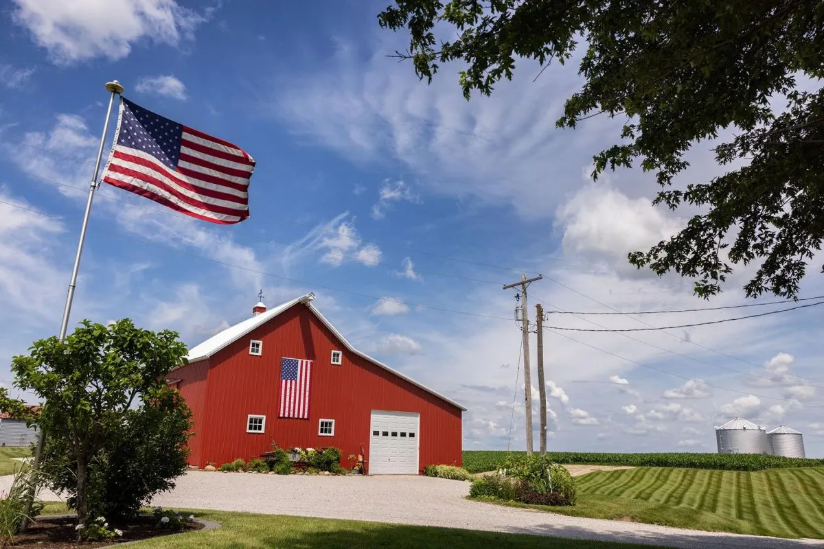 An American flag flying beside a red barn and green pasture